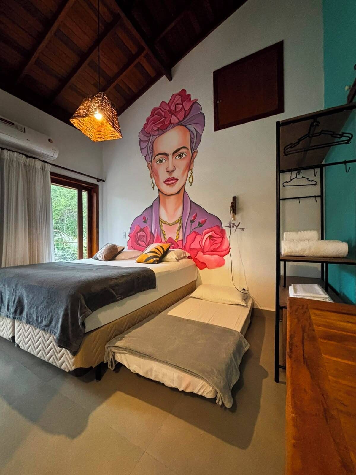A bedroom with a bed, a hanging light fixture, a wall-mounted shelf with towels, and a window with curtains.