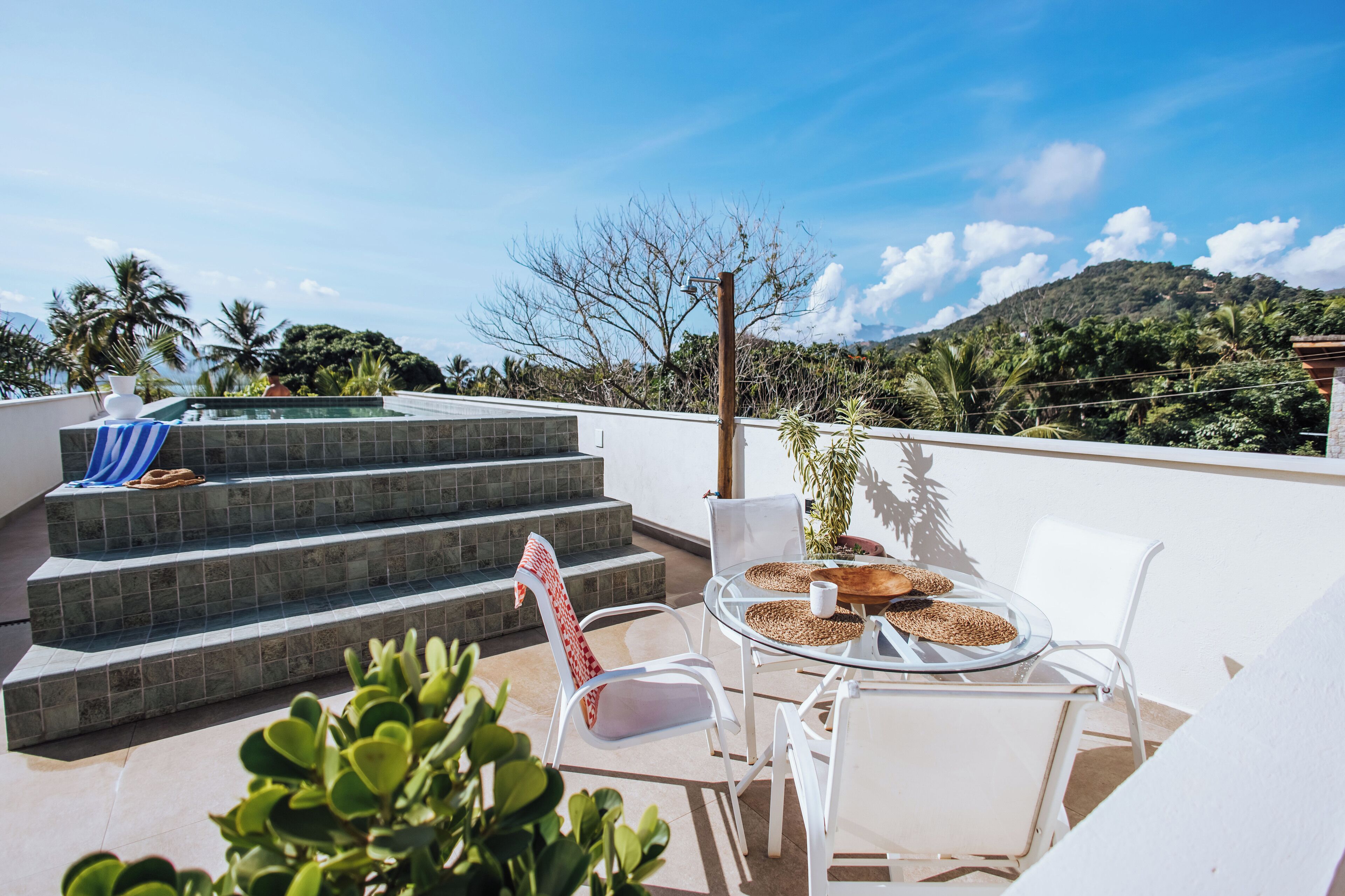 A rooftop terrace with a pool, white chairs, and a table with a woven placemat.