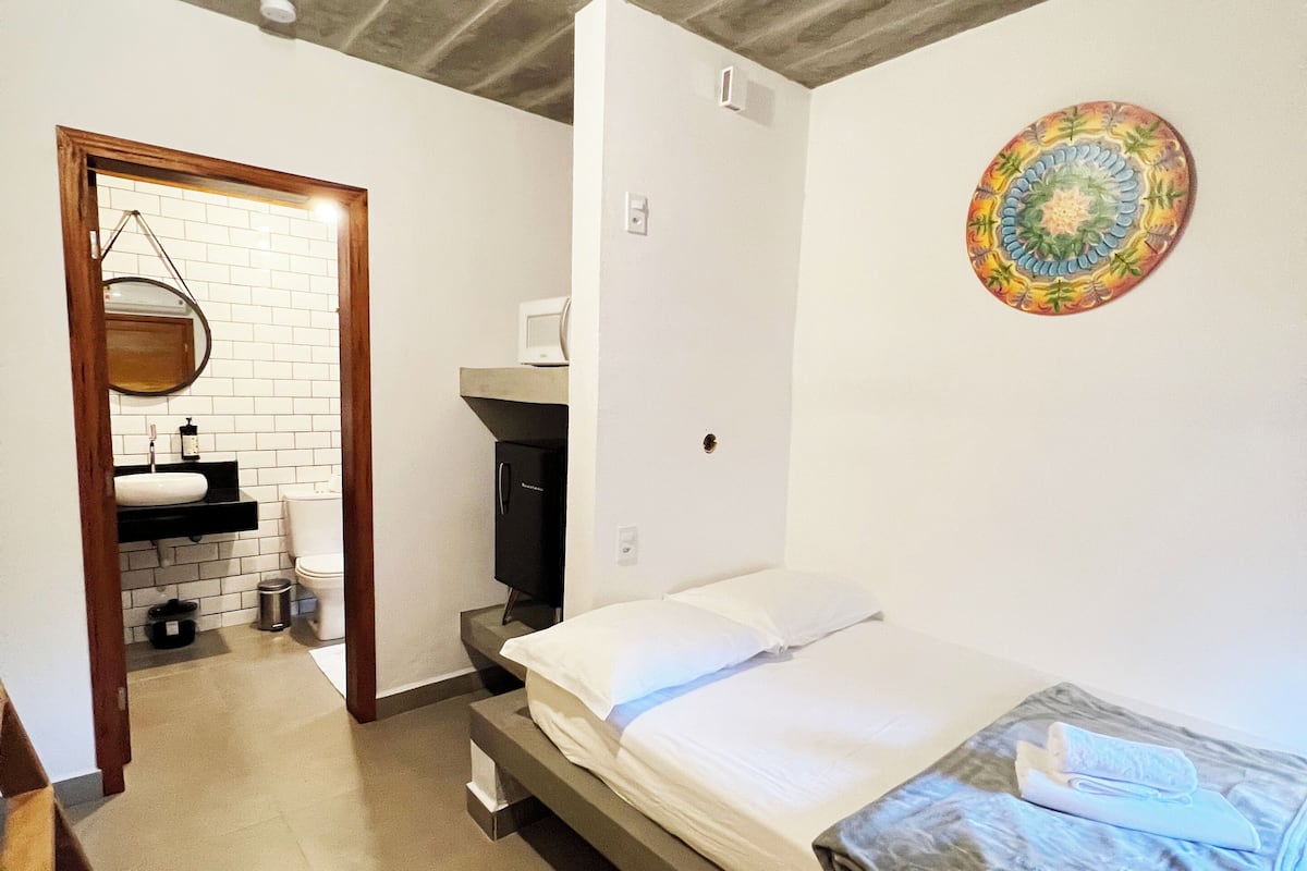 Un dormitorio con cama, una mesita de noche pequeña, un televisor montado en la pared y una lámpara de techo.