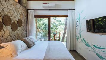 Una camera da letto con un letto, parete in pietra, condizionatore d'aria e vista sul verde attraverso una porta in vetro.
