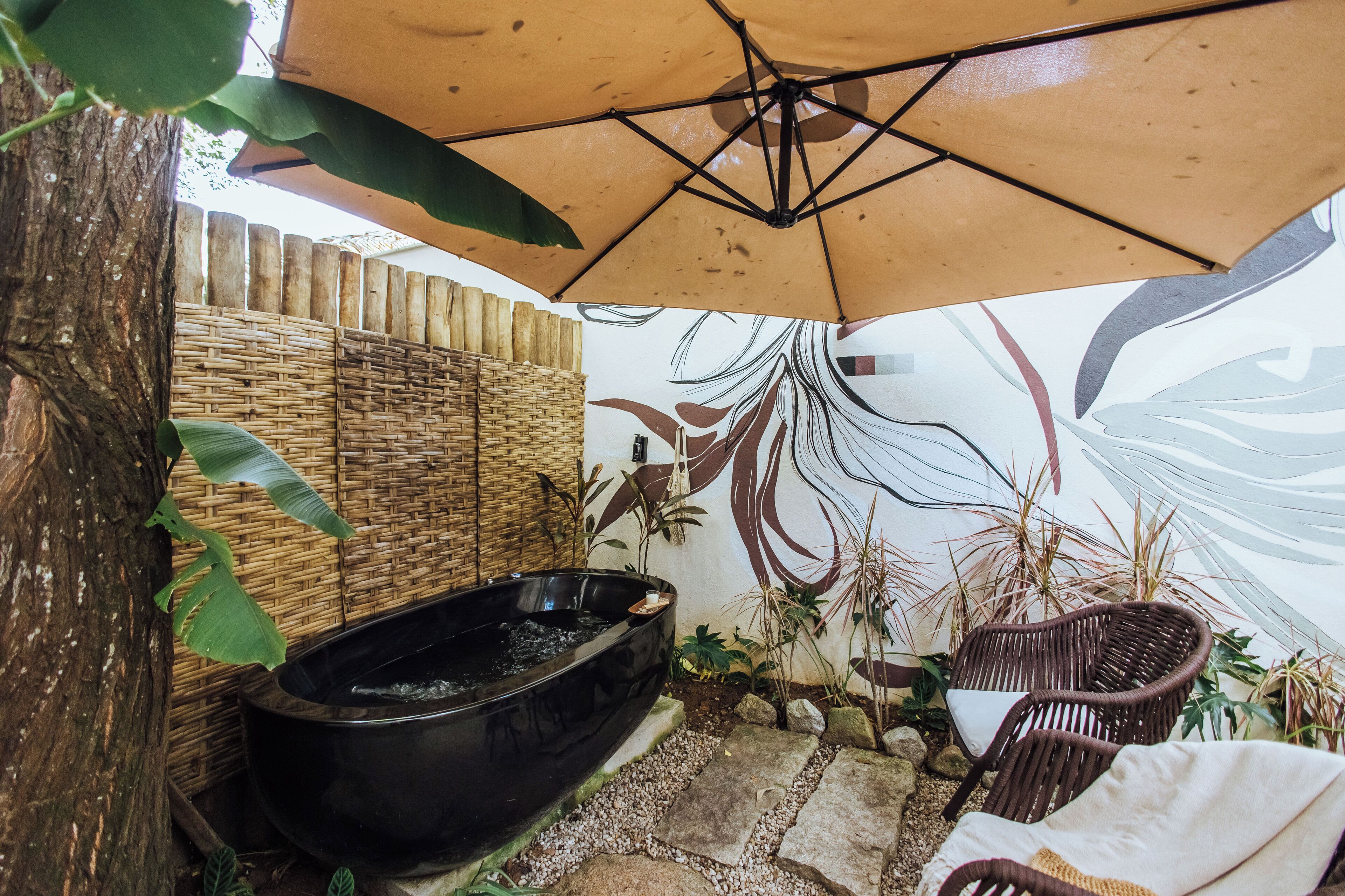 Un espacio exterior tranquilo con un jacuzzi negro, mobiliario de mimbre y una pared decorativa.