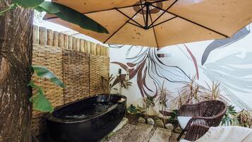 Un espacio exterior tranquilo con un jacuzzi negro, mobiliario de mimbre y una pared decorativa.