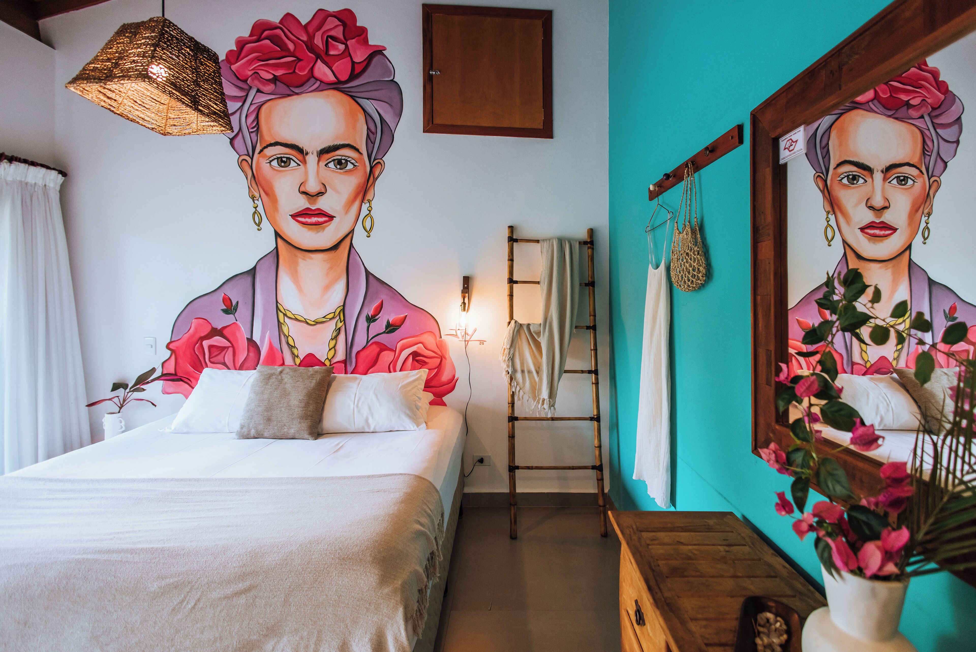 A bedroom with a large bed, a wooden dresser, a mirror, and a wall mural.