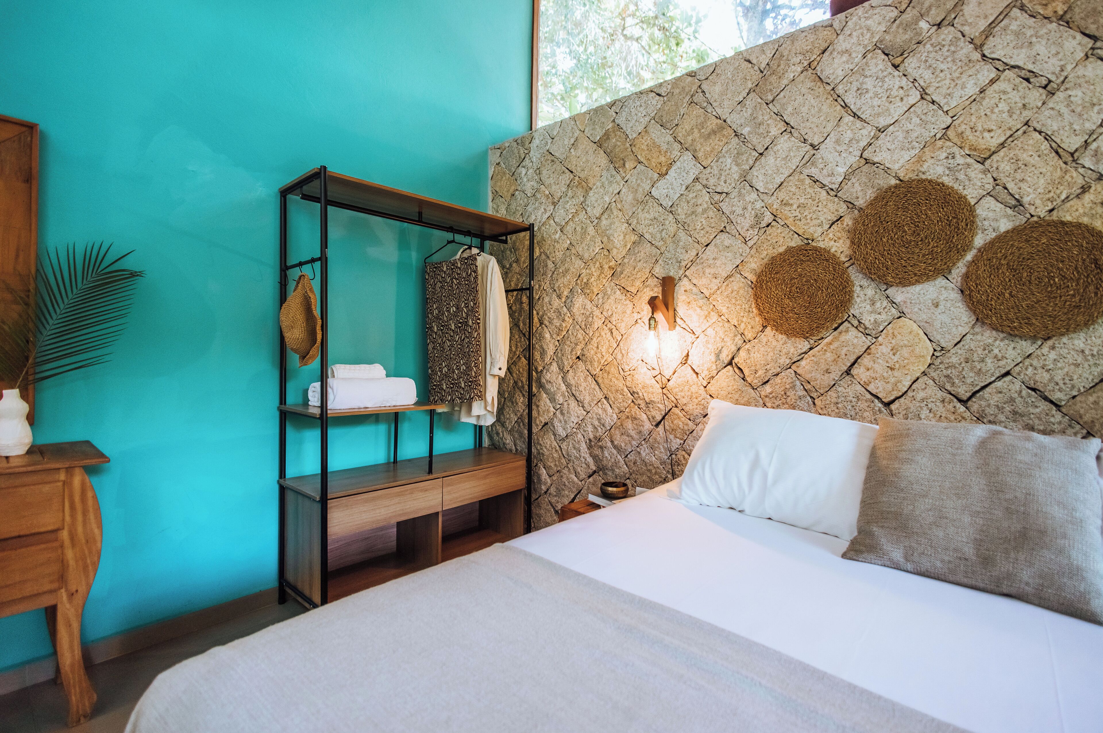 A bedroom with a bed, a wooden nightstand, a shelf unit, and a stone wall with circular decorations.
