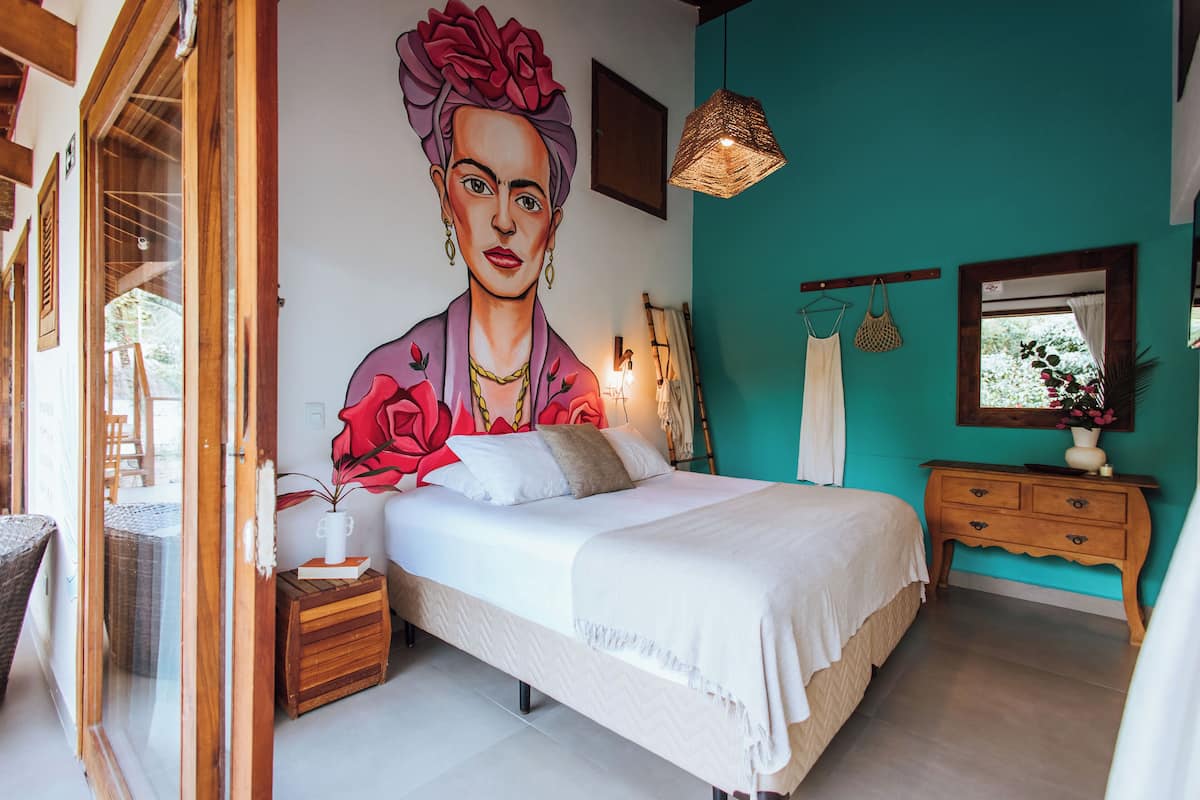 Un dormitorio con un mural grande, una cama, una mesita de noche, un aparador y una lámpara colgante.
