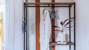 Une pièce avec une étagère en bois sur laquelle sont posés un vase blanc et un livre, un manteau accroché et un sac à motifs bleus et blancs.