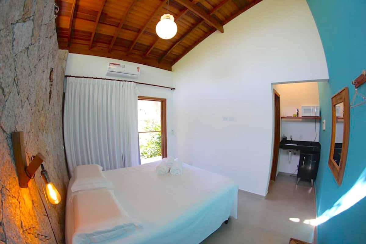 Un dormitorio con cama, ventana con cortinas, kitchenette y pared de piedra.
