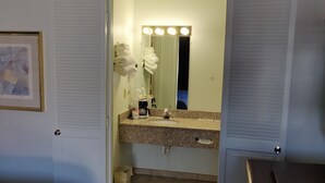 A hotel bathroom with a vanity, sink, and mirror with lights. There is a towel rack with towels, a trash can, and a framed picture on the wall. - Travel Inn Delaware (Delaware)