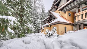 A snow-covered pathway leading to a building with a traditional architectural style, surrounded by snow-laden trees. - Stoney Creek Sunpath by Vacasa (Whistler)
