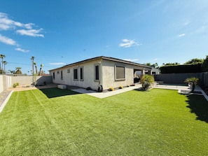 A single-story house with a well-maintained lawn, a small garden, and a clear sky.