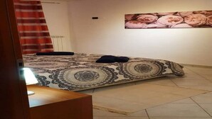 Um quarto com colcha estampada, uma obra de arte floral na parede e cortina listrada em vermelho e branco.