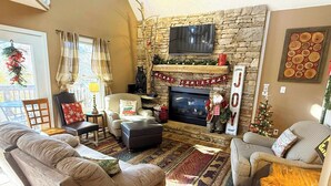 Una sala de estar acogedora con chimenea de piedra, un televisor montado encima y adornos navideños.