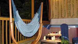 Un sillón hamaca, una mesita con velas y vasos, y una terraza de madera.
