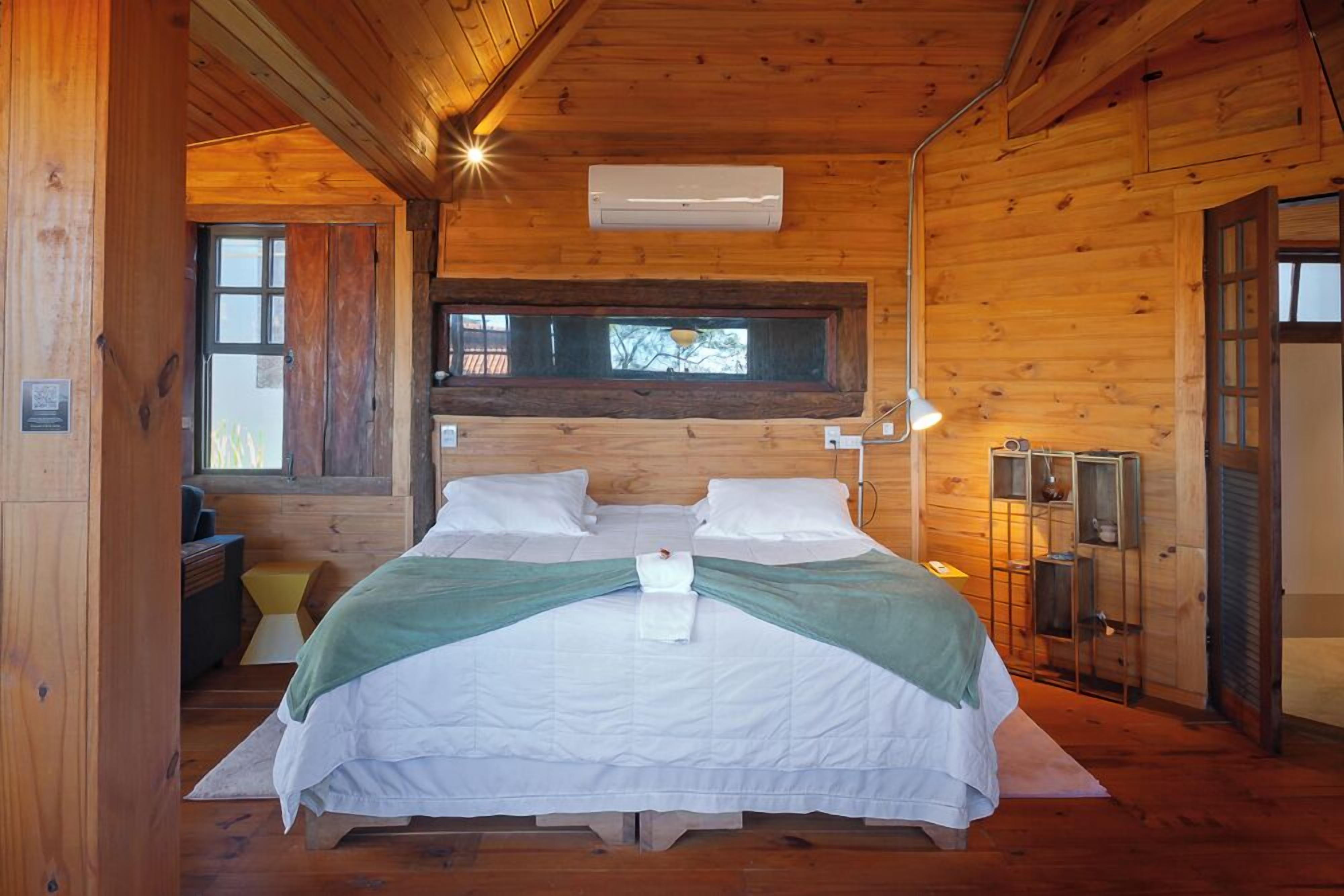 A wooden cabin bedroom with a bed, bedside lamp, and a window.