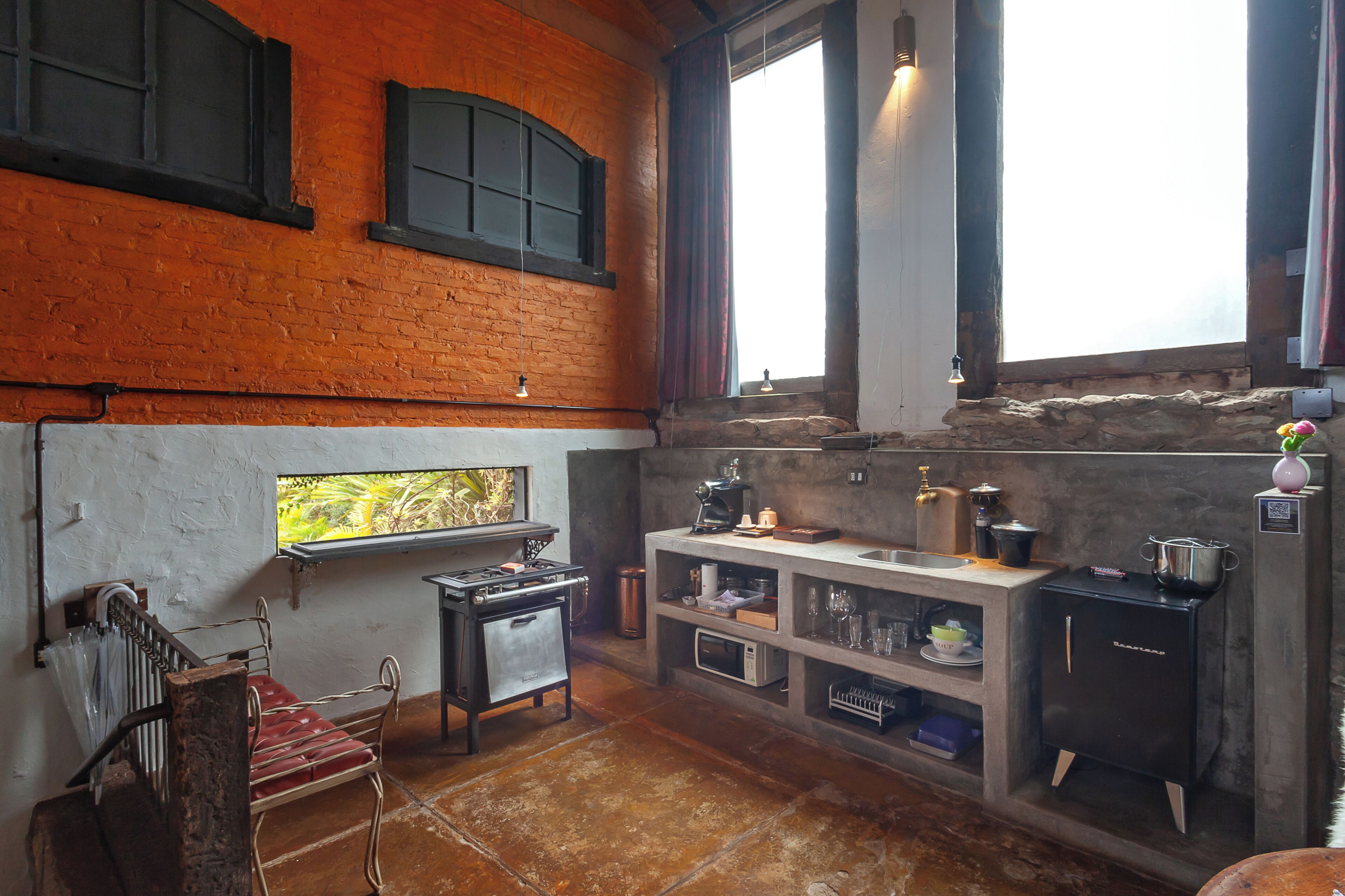 Una cocina rústica con pared de ladrillo, una ventana con cortinas, estufa empotrada y zona de lavabo.