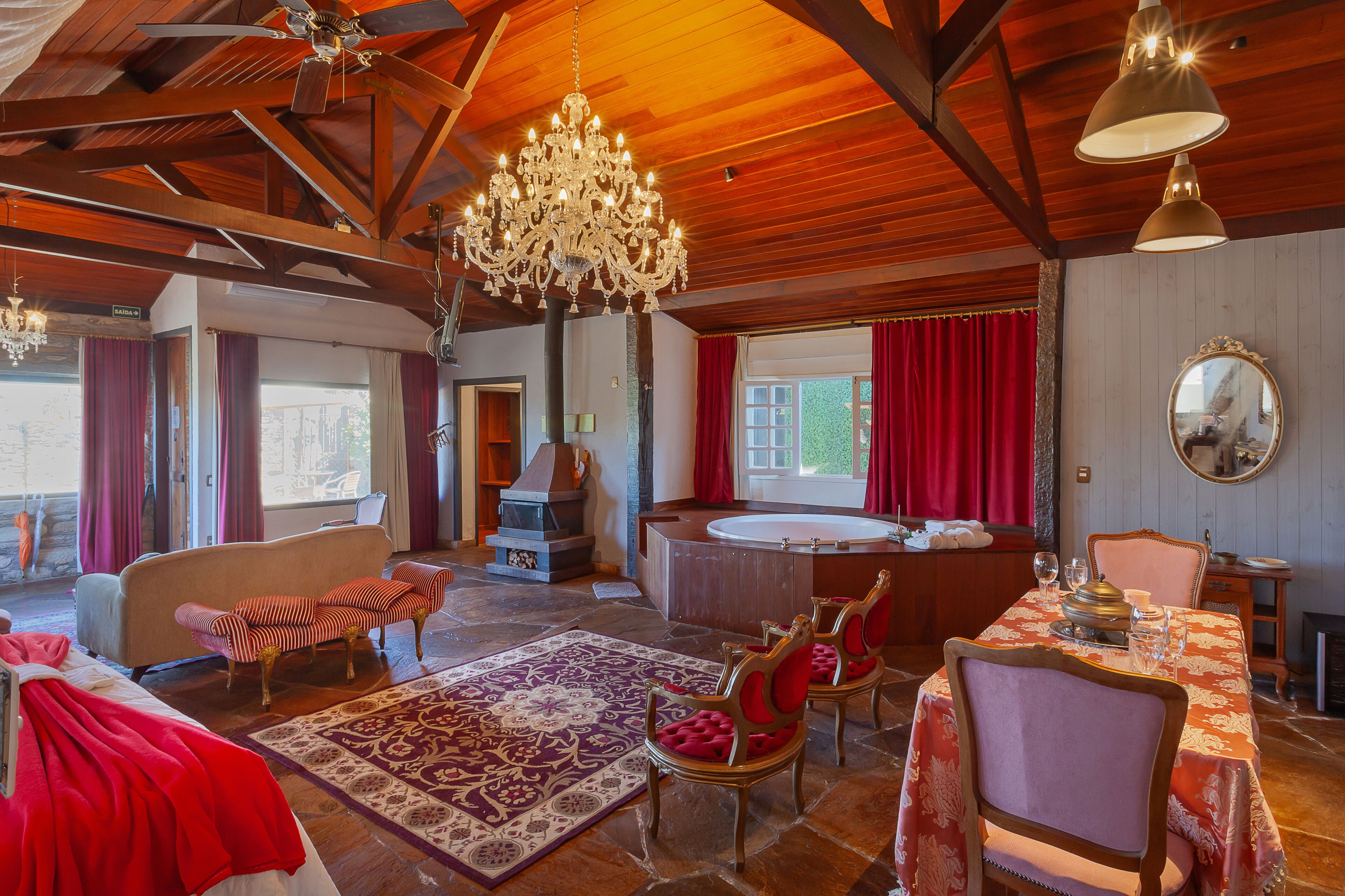 A spacious room with a large chandelier, a bathtub, and a dining area with a table set for two.