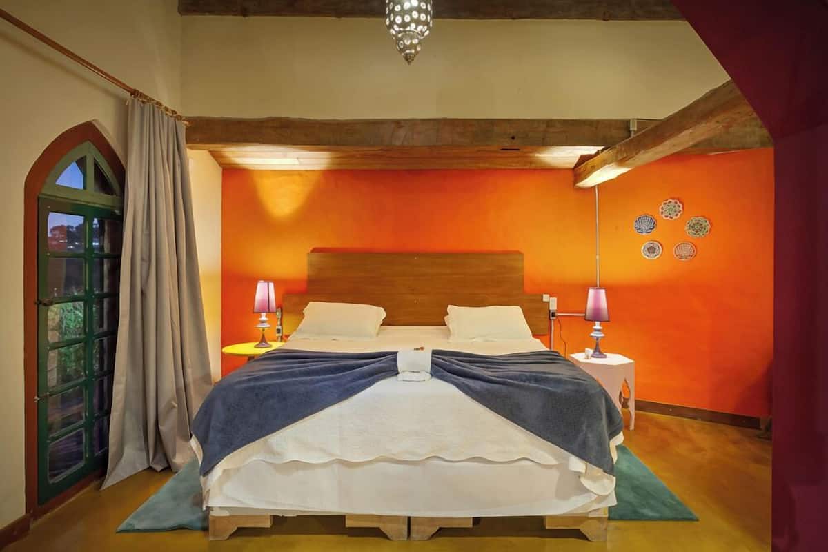 A bedroom with a wooden bed, two bedside tables with lamps, a chandelier, and a door with curtains.