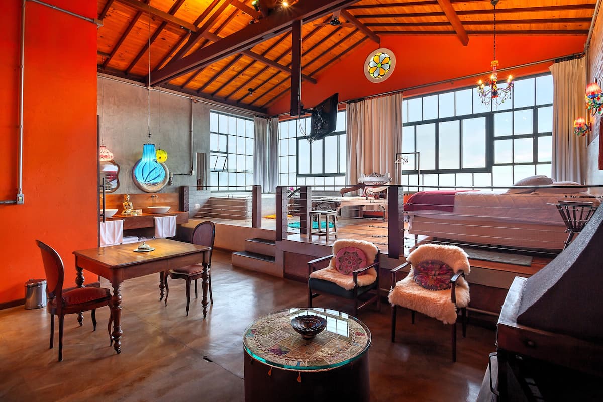 A spacious living area with a wooden ceiling, a piano, a dining table with chairs, and a large window providing natural light.