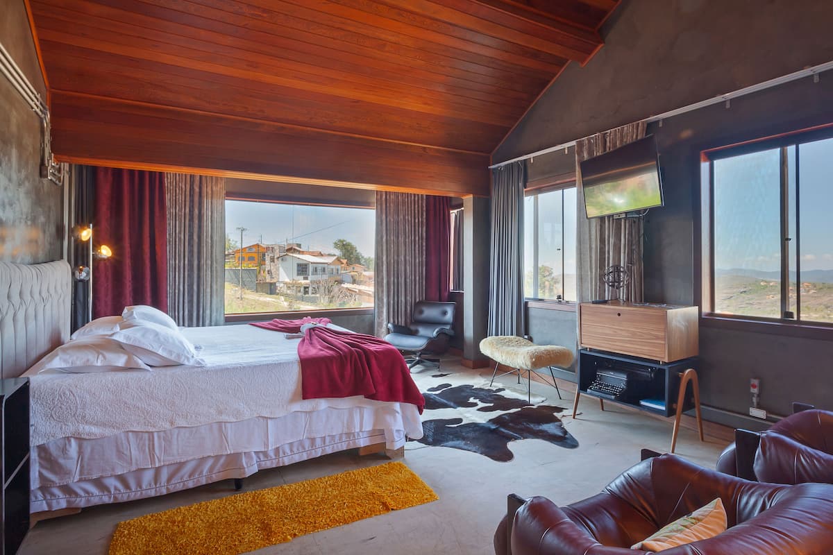 A bedroom with a large bed, a TV, a leather sofa, and a view of the outside.
