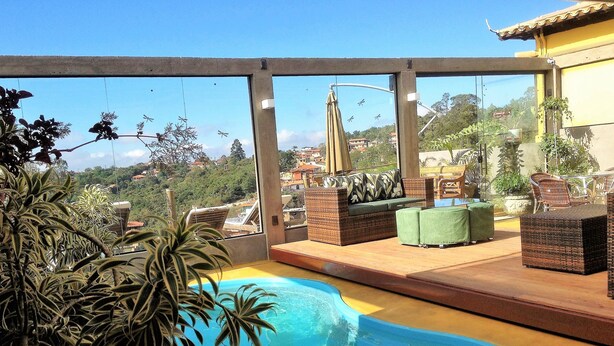 Uma área de piscina no terraço com vista para a cidade, móveis de vime e plantas em vasos.