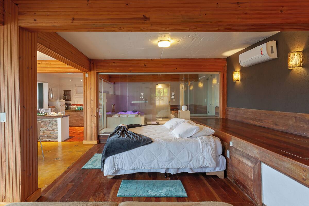 A bedroom with a bed, wooden floor, and a view into the kitchen.