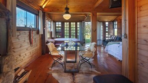 Interior de uma cabana de madeira com uma mesa de jantar, cadeiras, um sofá e uma cama.