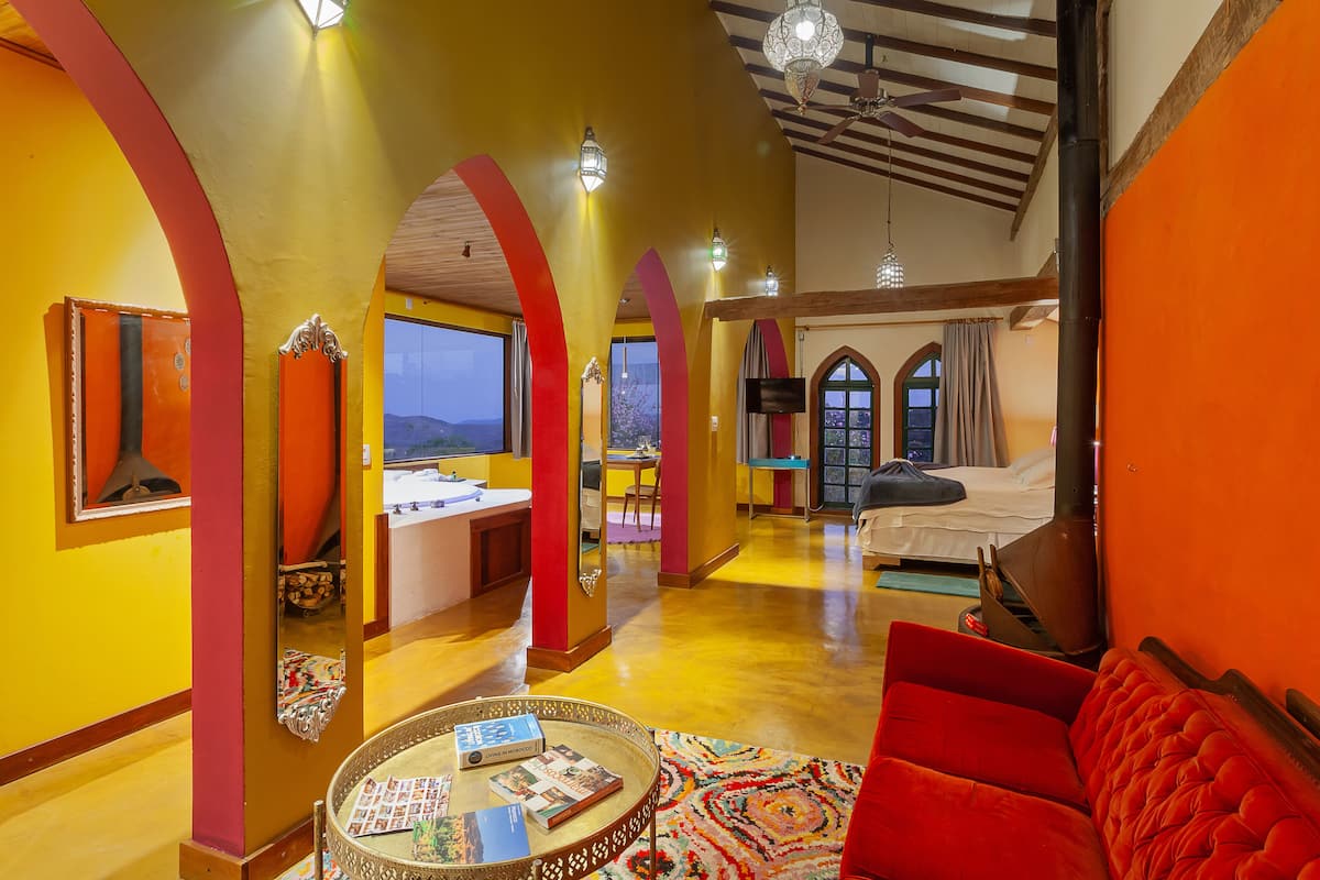 A spacious hotel room with a large bed, a red sofa, and a dining area with a view of the mountains.