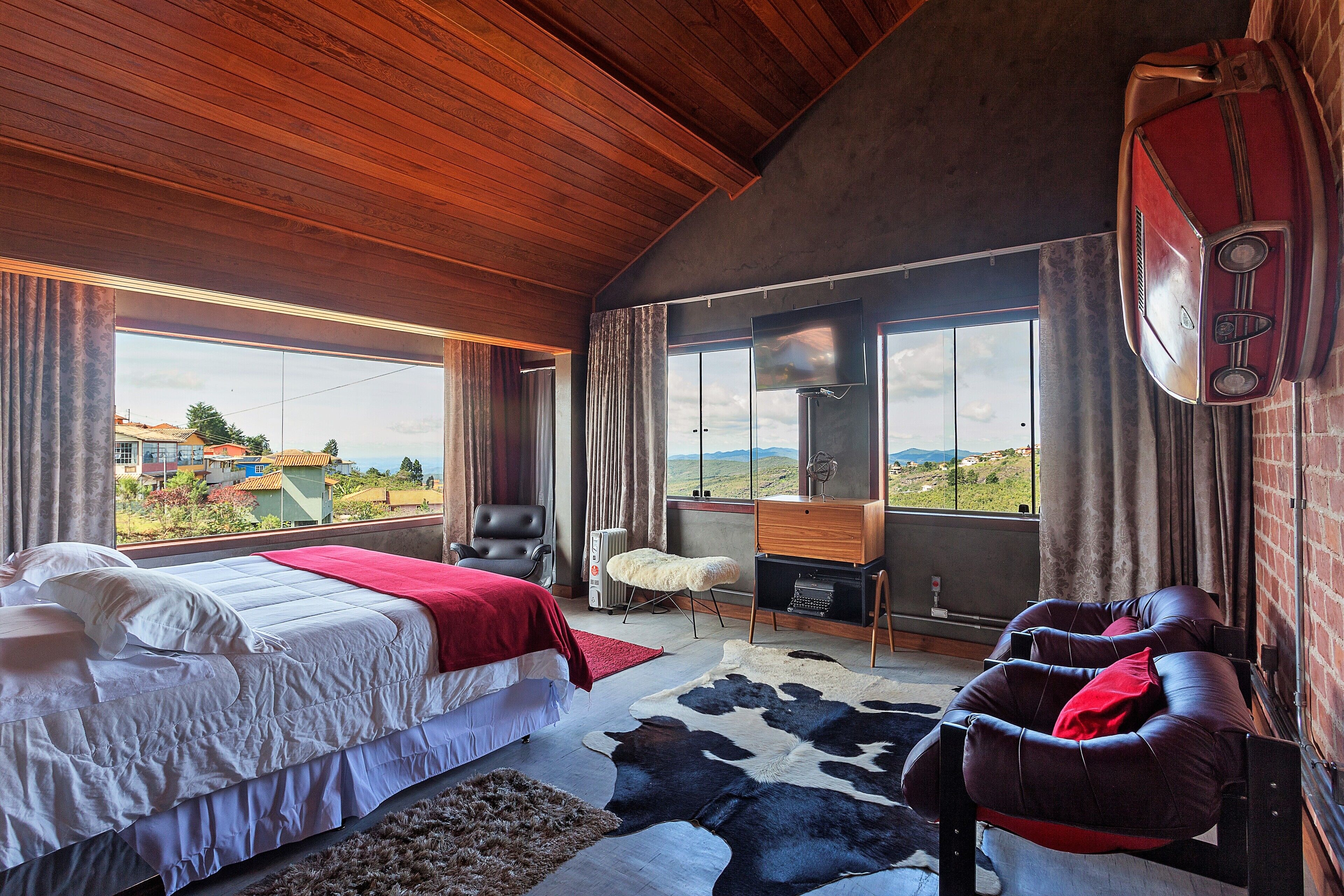 Un dormitorio con cama, escritorio, silla, alfombra de cuero de vaca y vistas al exterior.