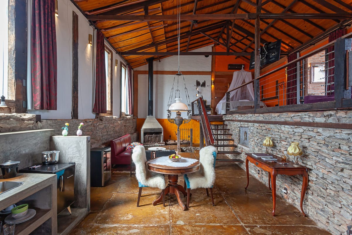A rustic kitchen with a stone wall, wooden beams, and a dining area with a round table and chairs.