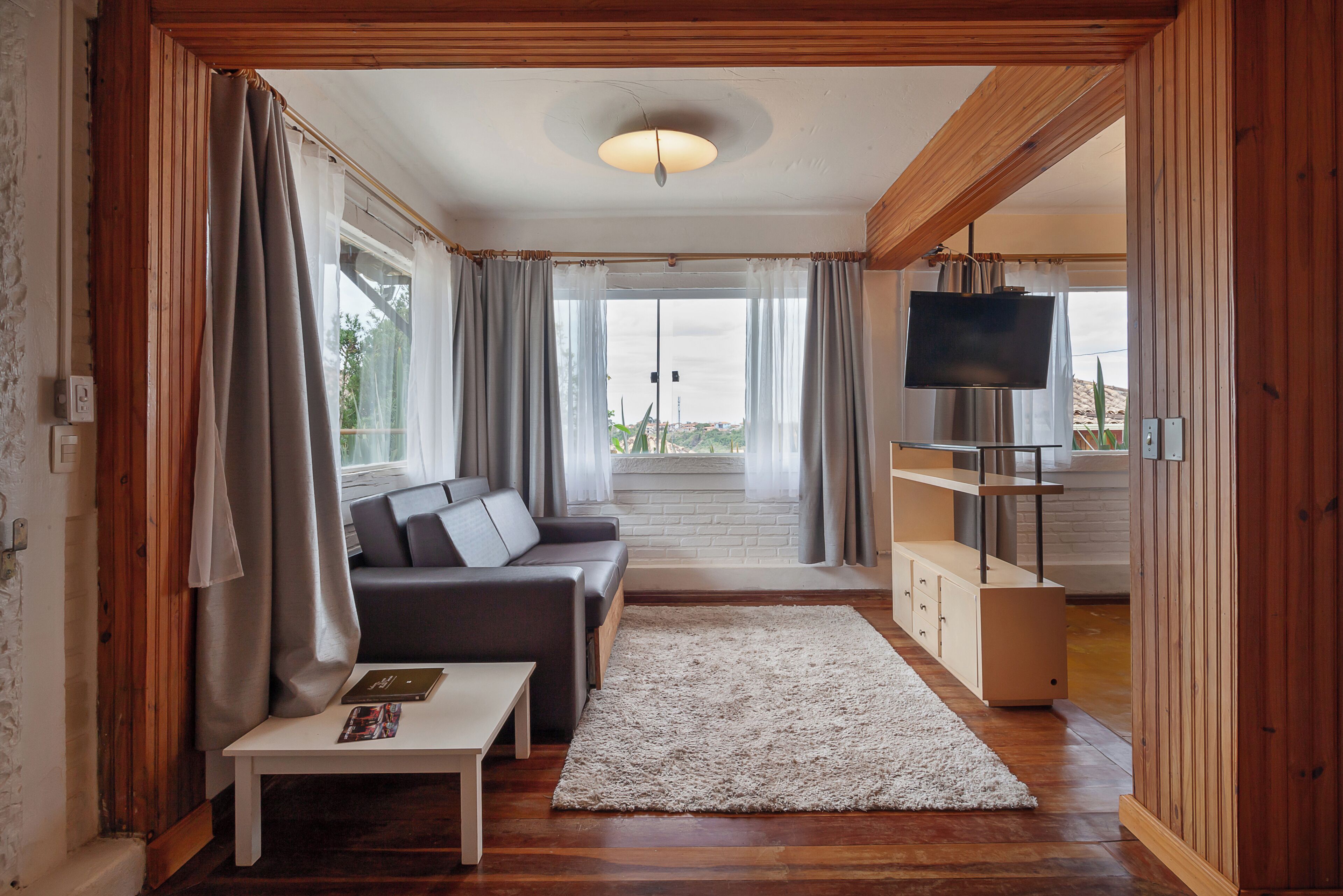 Ein Wohnzimmer mit einer Couch, einem Couchtisch, einem Fernseher und Blick ins Freie.