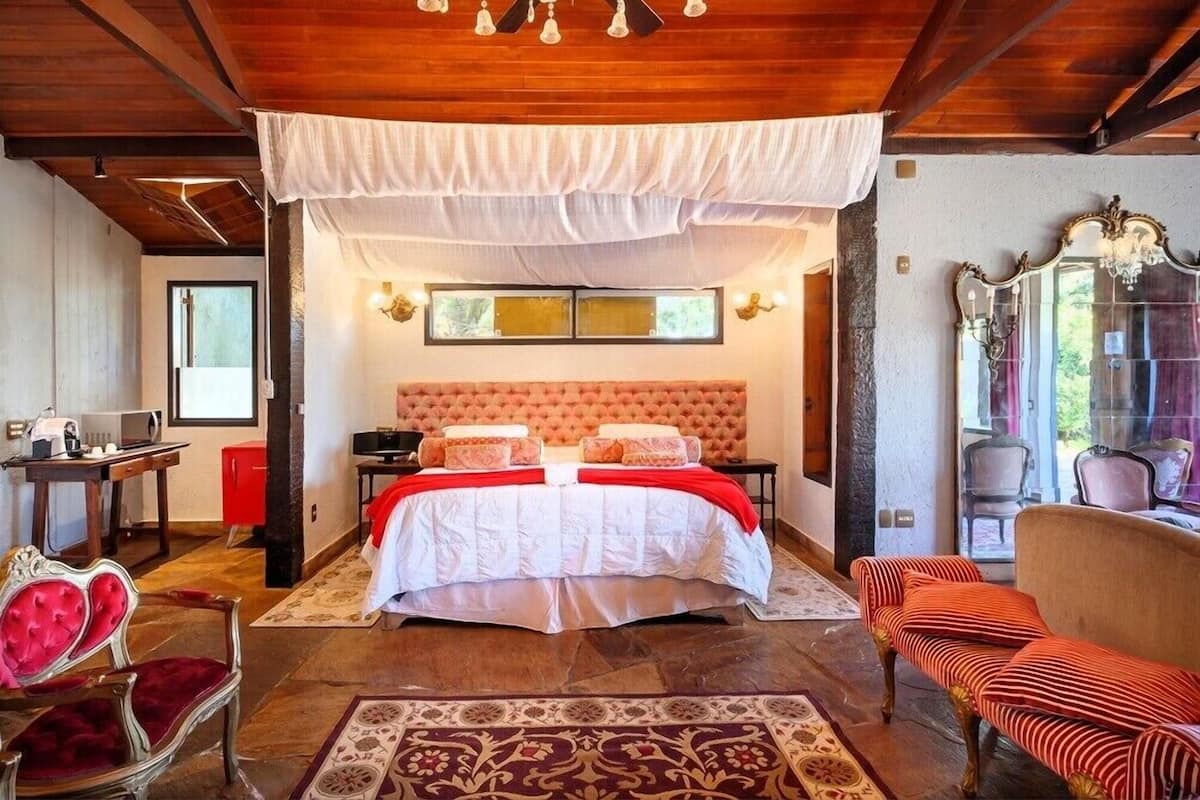 A bedroom with a large bed, a wooden ceiling, a chandelier, a mirror, and a red and white striped sofa.