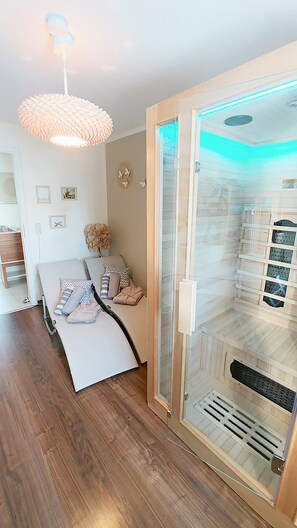 A bedroom with a bed, a bedside table, a wall-mounted lamp, and a sliding glass door leading to a bathroom with a shower.