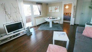 A modern living room with a flat-screen TV, a statue, a dining table with chairs, and a cozy seating area with a pink rug. - Feel-good time in the Zittau Mountains (Eichgraben)