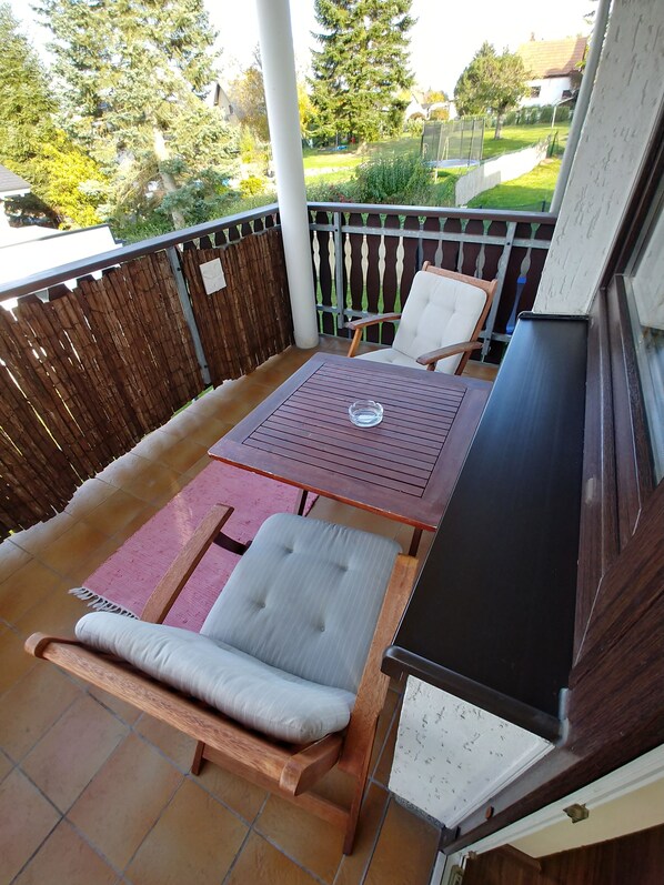 A patio with a table and two chairs, a wooden bench, and a view of a garden and houses in the background.