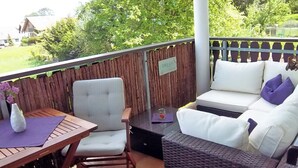 A patio with a wooden table, a cushioned chair, a wicker sofa, and a small table with a candle. - Feel-good time in the Zittau Mountains (Eichgraben)