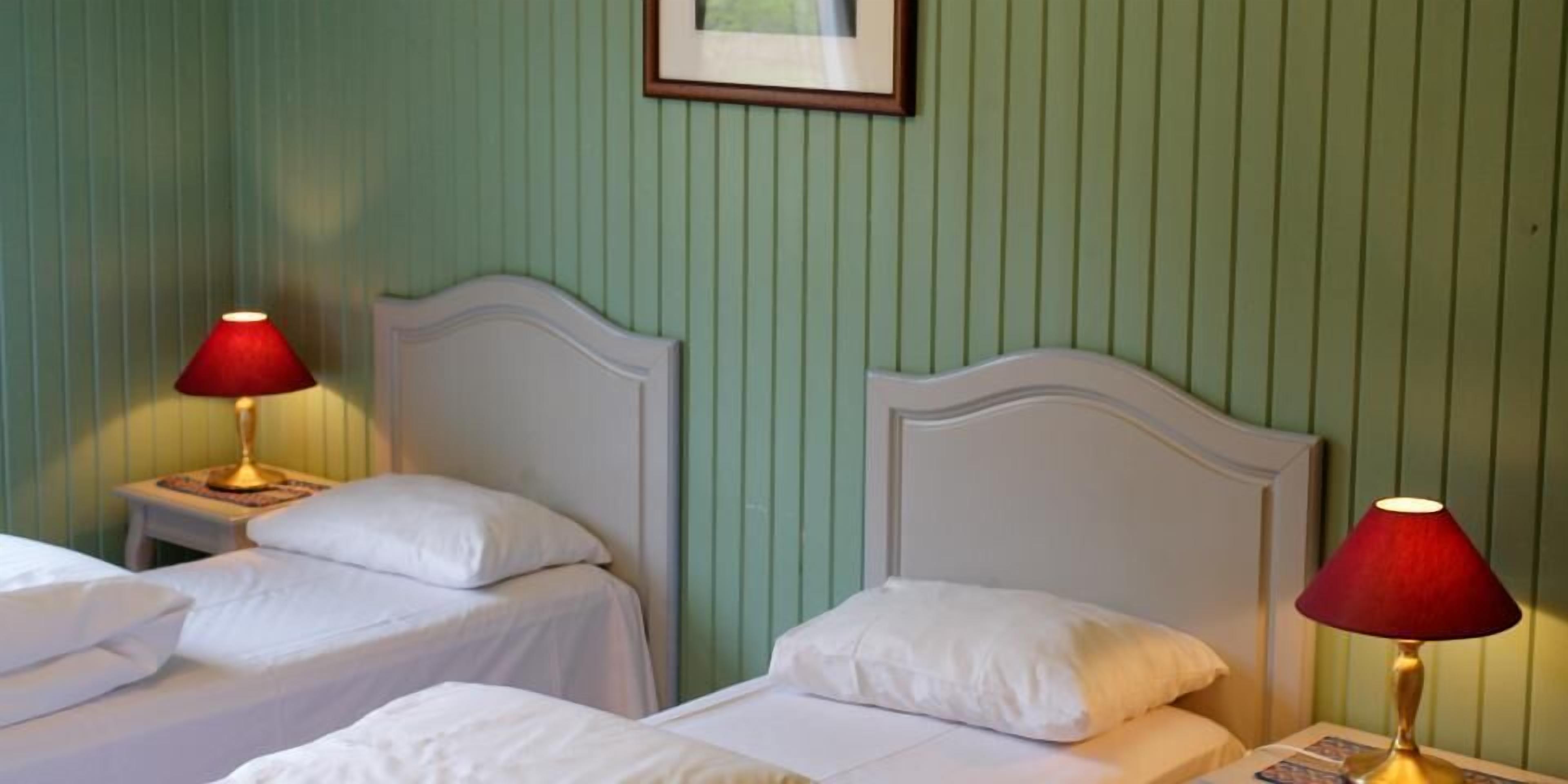 Una habitación de hotel con dos camas individuales, cada una con cabecero blanco y una lámpara roja sobre una mesita de noche.