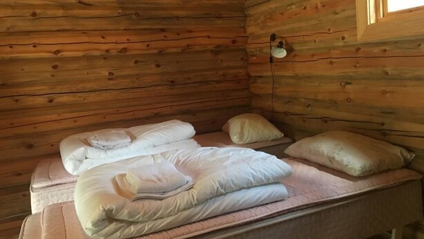 A cabin with two beds, each with pillows and blankets, a small window, and a wall-mounted light fixture.