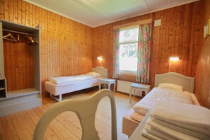 A room with wooden walls, two beds, a small table, and a chair.