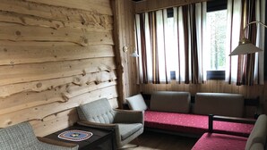 L'interno accogliente di un rifugio con parete in legno, un divano, due poltrone, un tavolino e una finestra con tende.