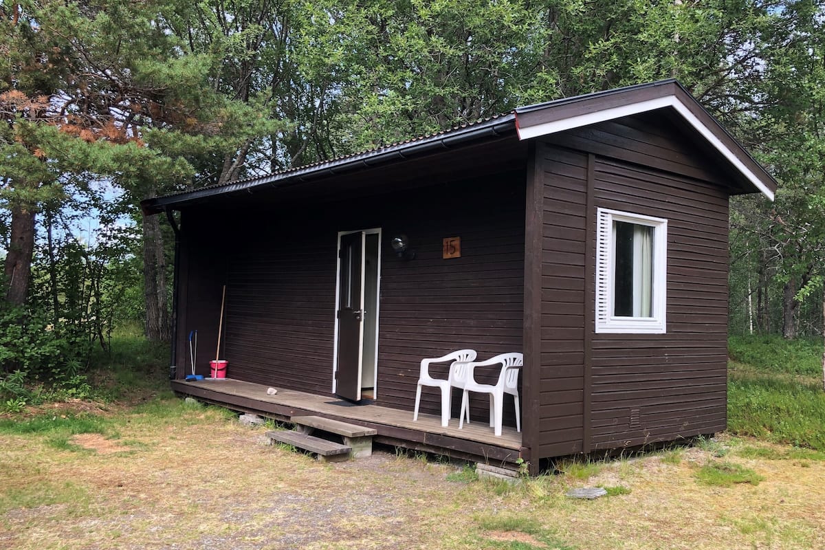 A small cabin with a porch, a door, and two white chairs.