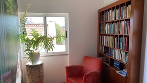 Une pièce avec une grande fenêtre, une bibliothèque, un fauteuil rouge et une plante en pot.