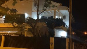 Une maison à deux étages avec un balcon, une cour clôturée et un arbre devant.