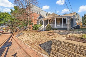 A residential house with a front porch, a brick driveway, and a stone retaining wall.