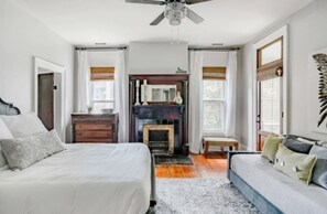 Cozy retreat with a large bed, dresser, and fireplace, complete with a ceiling fan and large window.