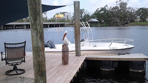 A wooden dock with a boat moored at the end, a chair, and a bird sculpture.