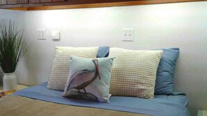 A bedroom with a bed, two pillows, a blue blanket, and a plant.