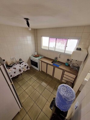A compact kitchen with a stove, sink, and window. - Apartment in Praia do Morro, 3 bedrooms, 2 suites (Guarapari)