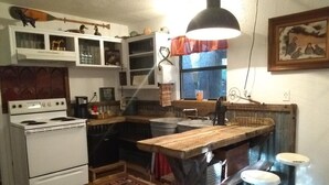Ett kompakt kök med en spis, en köksö i trä, barstolar och en hängande lampa.