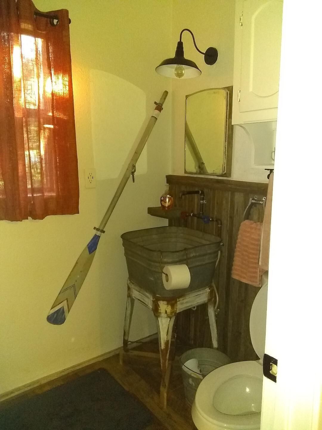 A bathroom with a toilet, a sink, a mirror, a shower, and a mop leaning against the wall.