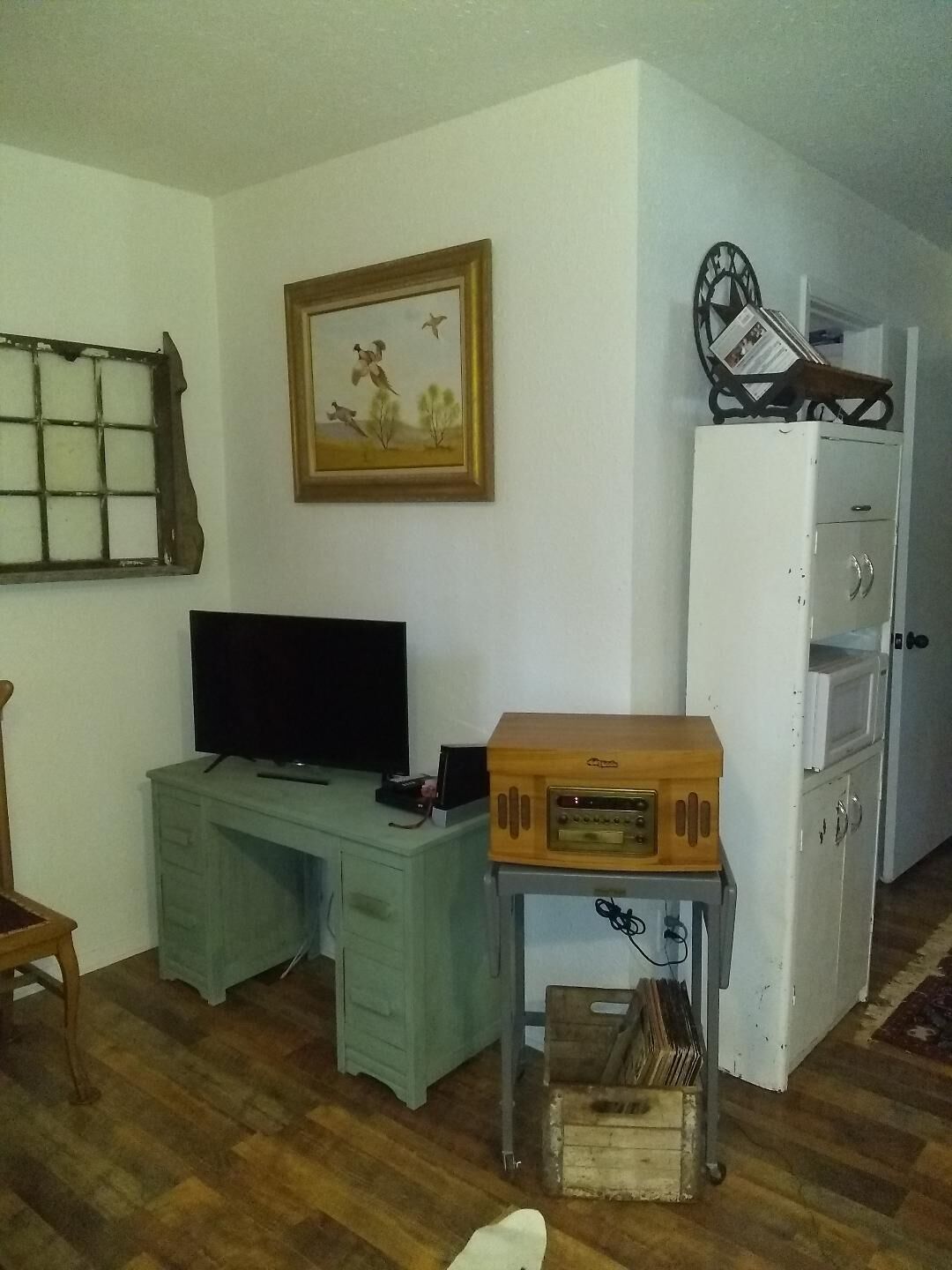 Une pièce comprenant un bureau en bois, un téléviseur, une armoire blanche et une petite table avec une radio.